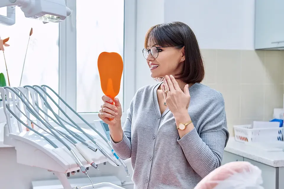 happy-woman-dentist-patient-with-mirror-in-hands Which Type of Dentist Performs Dental Implants: The Short Answer