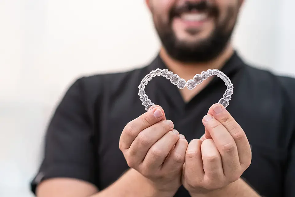 smiling-doctor-holding-heart-made-of-clear-aligner Is Invisalign Effective for Adults?: Common Pitfalls (And How We Avoid Them)
