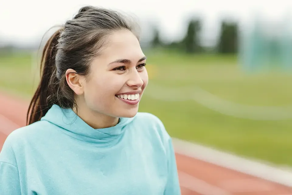 smiling-woman-in-a-blue-hoodie-at-the-track-field Is It Safe to Play Sports with Invisalign: Mouthguards That Actually Work